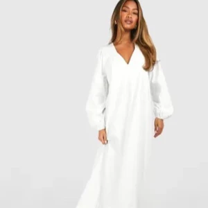 Vit långklänning med v-ringning - Snygg vit långklänning med v-ringad hals och långa puffärmar. Klänningen har en lös passform och volangdetalj längst ner, vilket ger en luftig och trendig look. Perfekt för dig som gillar stilrena och enkla plagg med en twist.