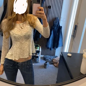 Vit spetsblus med lång ärm - Supersöt vit blus i spets med lång ärm och lätt utsvängd nederkant. Blusen är croppad och har ett blommigt spetsmönster som ger en romantisk vibe. Perfekt att styla med jeans eller kjol för en trendig look. 