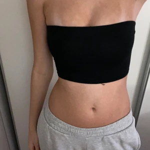 Svart bandeau tubtopp - Enkel och stilren svart bandeau tubtopp som sitter tight och är perfekt till varma dagar. Toppen är ärmlös och axelbandslös, med en croppad passform. Gjord i mjukt och stretchigt material för en bekväm känsla.