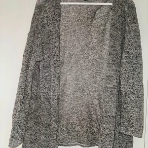 Gråmelerad kofta från H&M Divided - Säljer en gråmelerad lång kofta från H&M Divided i storlek M. Koftan är öppen framtill, har lång ärm och är tillverkad i en mjuk blandning av polyester, viskos och elastan. Perfekt att slänga över en t-shirt eller topp.