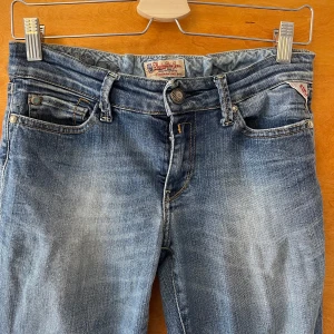 Replay jeans med broderi och slitningar - Snygga blå jeans från Replay med broderade blommor på bakfickan och coola slitningar. Klassisk femficksmodell med normal passform och raka ben. Jeansen har en ljus tvätt och detaljerade sömmar, perfekta för en avslappnad stil.