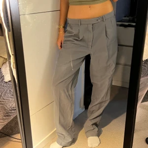 Grå lowwaist kostymbyxor - Snygga grå kostymbyxor med klassisk passform och pressveck. Byxorna har hällor för bälte, knäppning fram och bakficka med knapp. Materialet är en mix av 55% polyester och 45% ull, vilket ger en skön känsla och stilren look. Passar PERFEKT på mig som är S som lågmidjade. Om du gillar highwaist bör du nog vara L