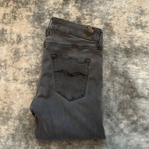 Grå jeans från Replay - Säljer ett par gråa slim fit jeans från Replay med klassisk femficksdesign och dragkedja. Jeansen har raka ben och diskreta sömmar på bakfickorna. Perfekta för dig som gillar en stilren look.