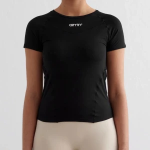 Svart AIM'N t-shirt i funktionsmaterial - Svart t-shirt från AIM'N med korta ärmar och rund hals. Tillverkad i ett stretchigt funktionsmaterial som andas, perfekt för träning. Diskret logga framtill i vitt. Snygg och sportig passform som sitter nära kroppen. Inte använd alls mycket!