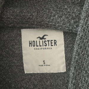 Grå kofta från Hollister, storlek S - Mysig grå kofta från Hollister i stickat material. Koftan har lång ärm, knappar framtill och två fickor. Perfekt för lager-på-lager och chill dagar. Snygg och enkel att matcha med det mesta.