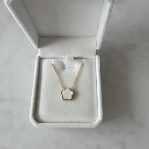 Halsband med blomma i pärlemor - Superfint halsband i med en söt blomformad berlock i vit pärlemor.