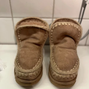 Beige boots från Mou i mocka - Säljer ett par beige boots från Mou med grova stickade detaljer längs kanterna. Skorna är tillverkade i mjuk mocka och har en platt sula, perfekt för kalla dagar. Klassisk rund tå och cozy vibes hela vägen.