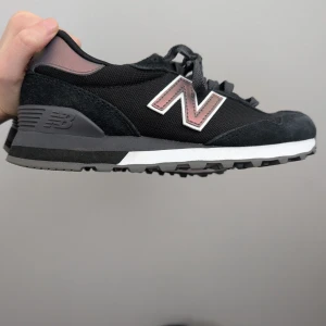 Svarta New Balance 515 sneakers - Snygga New Balance 515 sneakers i svart med detaljer i rosa metallic och grått. Ovandel i textil och mocka, grov mönstrad sula för bra grepp och klassisk N-logga på sidan. Skorna har snörning och bekväm innersula för extra komfort. 36