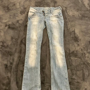 Ljusblå lågmidjade bootcut jeans från Fishbone - Snygga ljusblå jeans från Fishbone med bootcut passform och slitna detaljer. Jeansen har klassisk femficksdesign, dubbla knappar i midjan och ljusa tvättade partier framtill och baktill. Perfekta för en avslappnad och trendig look.