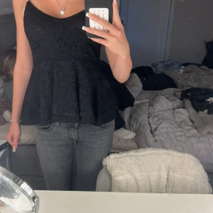 Svart spetslinne från Gina Tricot - Supersnygg svart linnetopp från Gina Tricot med tunna axelband och v-ringning. Toppen har ett peplumfall och är helt täckt av spetsdetaljer som ger en romantisk vibe. Perfekt att styla med jeans eller kjol för en trendig look.