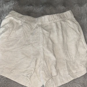 Beige linneshorts från H&M Divided - Snygga beige shorts från H&M Divided i luftig linnemix. De har elastisk midja för extra komfort och en avslappnad passform. Perfekta för varma dagar när du vill ha en chill och stilren look.