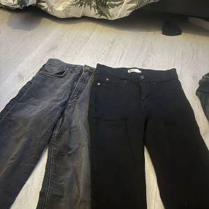Svarta och grå jeans från Domino - Två par jeans från Domino, ett par svarta och ett par grå. Båda har klassisk femficksdesign, raka ben och normal passform. Jeansen är tillverkade i stretchig bomullsdenim och har snygga detaljer som nitar och logga på bakfickan. Båda för 79 kr.