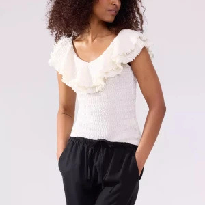 Vit volangtopp från Lindex - Supersöt vit topp från Lindex med volanger runt halsen och axlarna. Smockad och stretchig i materialet, ärmlös och med v-ringad front. Storlek M men skulle säga att den passar S också. Originalpris: 400kr. Bara använd 1 gång