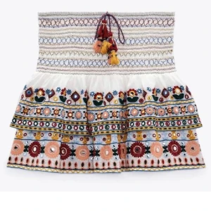 Broderad vit kortkjol med volanger från Zara - Superfin vit kortkjol med broderade blommor i rött, rosa, blått, gult och grönt. Kjolen har volanger, snörning med tofsar i midjan och färgglada detaljer. Perfekt till sommaren och skolan!❤️🌺(lånade bilder)