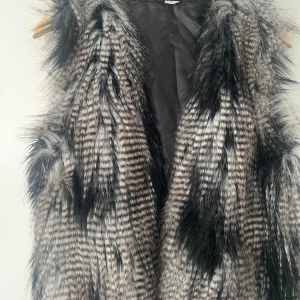 Randig pälsväst från H&M Divided - Säljer en fluffig och cool pälsväst från H&M Divided i storlek 40. Västen har ett randigt mönster i svart och grått med långa, mjuka strån som ger en edgy vibe. 