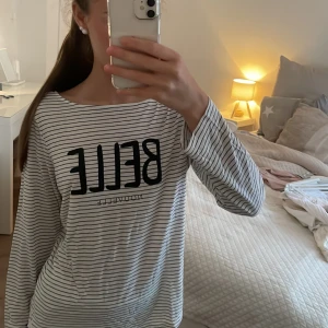 Randig långärmad tröja från H&M - Säljer en vit och svart långärmad tröja från H&M med tunna horisontella ränder och trycket 'BELLE NOUVELLE' framtill. Tröjan har en avslappnad passform och är gjord i mjuk bomull. Rund halsringning och klassisk look.