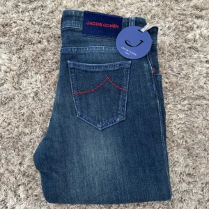 Jacob Cohën blå jeans straight fit - Snygga blå jeans från Jacob Cohën med klassisk femficksdesign och röda detaljer på bakfickorna. Jeansen har en rak passform och är tillverkade i mjukt denimtyg som sitter skönt hela dagen. Perfekta för dig som gillar stilrena och tidlösa jeans. Helt sprillans nya helt oanvända med lappar kvar. Ny pris på dessa är 4000kr. Priset kan diskuteras. Passar en 13 åring ca 156-160 cm