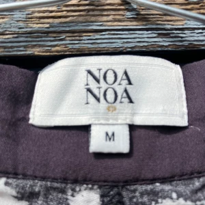 Svart & vitmönstrade byxor från Noa Noa - Säljer ett par svarta byxor från Noa Noa i storlek M med vitt prickigt mönster. Byxorna har en avslappnad passform, knapp och dragkedja framtill samt sid och bakfickor. Materialet känns lätt och luftigt, perfekt för dig som gillar en chill och unik stil.