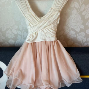 Ljusrosa omlottklänning med volang, stl xs-s - Superfin kortklänning i ljusrosa och vitt med omlottliv och volangkjol. Överdelen har snygga draperingar och breda axelband.