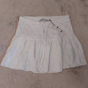 Vit broderad kortkjol från 157 - Supersöt helt ny vit kortkjol från 157 i storlek XS. Kjolen har broderade detaljer och ett volangformat fall som ger en chill och feminin vibe. Den har snörning i midjan för extra passform och är gjord i bomull, perfekt för varma dagar.