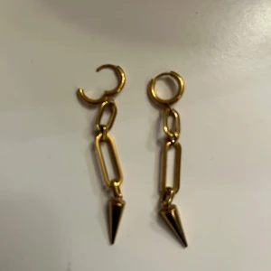 Guldiga örhängen med kedjor och spikes - Snygga guldiga örhängen med cool kedjedesign och spetsiga spikes längst ner. Perfekt för dig som gillar statement-smycken med edgy vibe. Hängande modell som ger extra attityd till din look. NY SKICK🩷