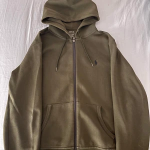 Zip tröja från ralph lauren - Snygg grön zip hoodie från Polo Ralph Lauren med dragkedja och huva. Klassisk logga broderad på bröstet, praktiska fickor framtill och snörning i huvan. 