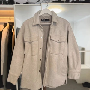 Beige overshirt från Zara - Snygg beige overshirt från Zara med klassisk krage och två stora bröstfickor med knappar. Jackan har lång ärm med knapp vid mudden och en loose passform som ger en chill vibe. Perfekt att slänga över en hoodie eller t-shirt för en laidback look.