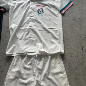 Casa Tennis Club vita shorts och vit tröja  - Vita shorts från Casa Tennis Club med elastisk midja och snörning. Materialet är mjukt och syntetiskt, perfekt för sport. Nedtill finns en turkos kant. Passar dig som gillar tennis och sportig stil.