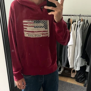 Röd hoodie från Ralph Lauren - Säljer en röd hoodie från Ralph Lauren Denim & Supply med stor amerikansk flagga-patch på bröstet. Tröjan har huva, känguruficka och långa ärmar. Perfekt för chill dagar. Snygg vintage-vibe! Strl m pris kan diskuteras 