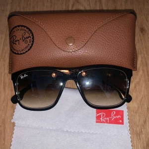 Svarta Ray-Ban solglasögon - Snygga svarta Ray-Ban solglasögon med fyrkantig form och tonade linser som går från mörkt till ljust brunt. Bågarna är i blank plast med guldfärgad Ray-Ban-logga på sidan. Medföljer original brunt fodral i skinn och putsduk.