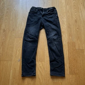 Svarta jeansbyxor från Lindex - Svarta jeansbyxor från Lindex med klassisk femficksdesign och raka ben. Byxorna har normal passform och är tillverkade i mjukt bomullsmaterial med lite stretch för extra komfort. Perfekt för dig som gillar en enkel och stilren look. Strl 152/164.