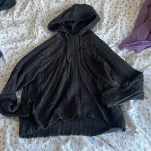 Svart stickad hoodie från Vero Moda - Mysig svart stickad hoodie från Vero Moda med ribbad struktur och snörning vid huvan. Tröjan har lång ärm och en lite loose passform, perfekt för chill dagar. Materialet är mjukt och ger en avslappnad vibe. Snyggt sliten kant nedtill för en cool look. den är i xs men oversize så skulle säga S