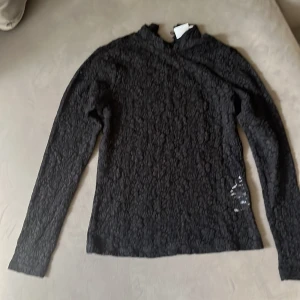 Svart spetsblus från VILA - Supersnygg svart blus från VILA med lång ärm och blommigt spetsmönster. Blusen har en liten öppning vid halsen och är gjord i ett tunt, elegant material som känns lyxigt. Perfekt för dig som gillar detaljer och vill ha något som sticker ut.