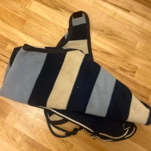 Ländtäcke Rambo  - Säljer ett ländtäcke Rambo Competition från Horseware med breda marinblå, ljusblå och vita ränder. Täcket är gjort i mjuk fleece och har praktiska detaljer som knytband och metallspännen. Perfekt för ridning under kyliga dagar.