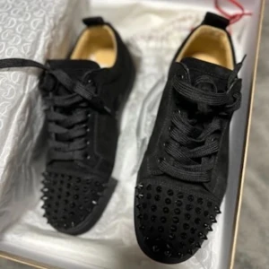 Christian Louboutin svarta sneakers med nitar - Svarta sneakers från Christian Louboutin i mocka med coola svarta nitar på tån och klassisk röd sula. Skorna har snörning och rund tå, vilket ger en edgy vibe. Perfekta för dig som vill sticka ut med exklusiv design och detaljer.