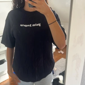 Svart Palm Angels t-shirt - Svart t-shirt från Palm Angels med vit logotyptryck både fram och bak i cool gotisk stil. Modellen är loose fit med korta ärmar och rund hals. 