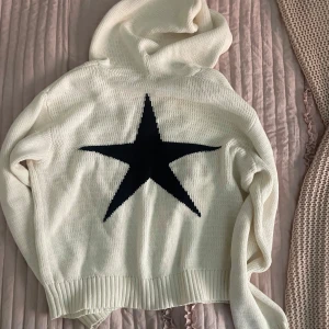 Vit hoodie med svart stjärna - Vit stickad hoodie med stor svart stjärna på ryggen. Tröjan har v-ringad hals, långa ärmar och ribbade muddar vid ärmslut och nederkant. Den är i barn storlek men passar mig som har S vanligtvis❤️