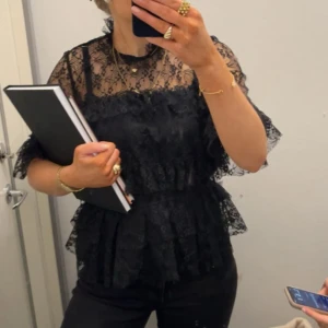 Svart spetsblus med volanger - Supersnygg svart blus i spets med transparent överdel och korta volangärmar. Blusen har volanger både vid midjan och ärmsluten, samt en rund halsringning. Storlek 38 och från bubbleroom. Nypris 499☺️