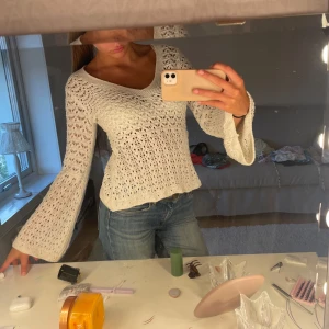 Vit stickad tröja med utsvängda ärmar - Superfin vit stickad tröja med v-ringning och utsvängda långärmar. Tröjan har ett luftigt hålmönster och sitter snyggt med en lite loose passform. Perfekt att styla med jeans eller kjol för en chill look.