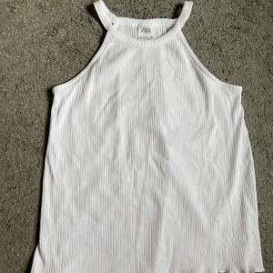 Vit ribbad linnetopp från Zara - Vit linnetopp från Zara med smala axelband och hög hals. Toppen har ett ribbat mönster som ger en snygg struktur och är tillverkad i mjuk bomull. Perfekt för dig som gillar enkel och clean stil.