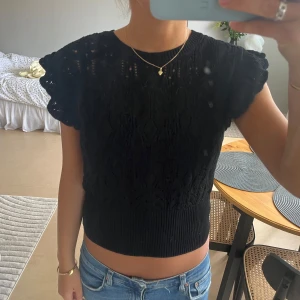 Svart stickad topp med volangärm Lindex - Säljer en svart stickad topp från Lindex i storlek M. Toppen har korta volangärmar och ett snyggt hålmönster över hela plagget. Ribbad kant nedtill och vid halsen. 