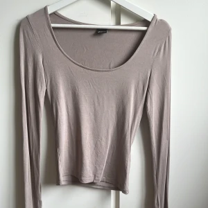 Beige långärmad croppad topp - Snygg beige långärmad topp från Stradivarius med croppad passform och rundad halsringning. Mjuk och stretchig bomullsmix som sitter skönt mot kroppen. Perfekt att styla med jeans eller kjol för en chill look.