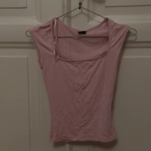 Ljusrosa ärmlös topp Gina Tricot - Supersöt ljusrosa topp från Gina Tricot i storlek XXS. Modellen är ärmlös med en snygg fyrkantig halsringning och smal passform. Materialet känns mjukt och stretchigt, perfekt för att styla med jeans eller kjol. Enkel och clean design som är lätt att matcha.
