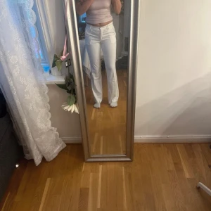 Vita bootcut byxor med fickor - Snygga vita bootcut byxor med fickor fram och bak, samt hällor för bälte. Byxorna har en högmidjad passform och raka ben med lätt utsvängning. Perfekta för dig som vill ha en clean och fräsch look. Materialet känns mjukt och följsamt.