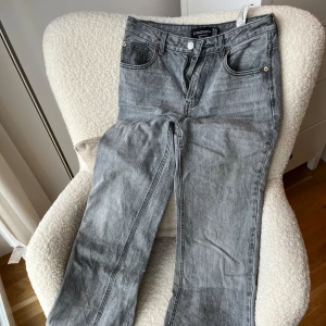 Grå jeans från Stradivarius, storlek 36 - Snygga grå jeans från Stradivarius i storlek 36. Modellen har klassisk femficksdesign, raka ben och wide passform. Jeansen är tillverkade i denim med en cool tvättad look och har knapp och dragkedja framtill. Perfekta för dig som gillar en chill och stilren vibe.