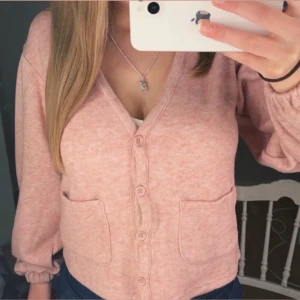 Ljusrosa kofta med fickor - Söt ljusrosa kofta med v-ringning och tre knappar framtill. Tröjan har två fickor och långa ärmar med resår vid handlederna. Perfekt för lager-på-lager och enkel att matcha med olika outfits.