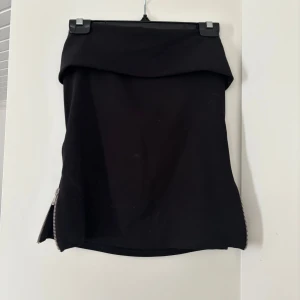 Svart tubtopp  med dragkedja - Säljer en svart tubtopp med coola dragkedjedetaljer på sidorna. Toppen har en enkel och stilren design med en tight passform som passar perfekt till många olika looks.