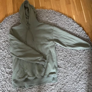 Grön hoodie från Pieces - Säljer en enkel och stilren grön hoodie från Pieces. Tröjan har huva med dragsko och en stor ficka framtill. Perfekt för en avslappnad look.