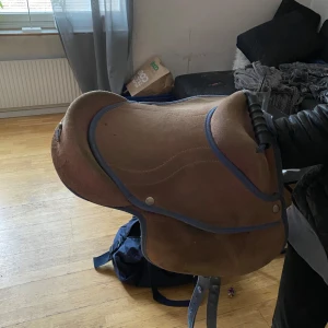 Brun hästsadel med blå kant -  Lägg bud Säljer en brun hästsadel med blå kant och dekorativa sömmar. Sitsen är mjuk och sadeln har metallbeslag. Perfekt för ridning och passar de flesta hästar. Sadelgjord ingår men  ingår i j tyvärr stigläder ingår ej.