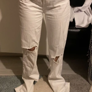 Vita jeans med hål på knäna - Säljer ett par vita jeans med raka ben och slitna hål på båda knäna. Byxorna har normal passform och är långa i modellen. Perfekta för dig som gillar en avslappnad och trendig stil.